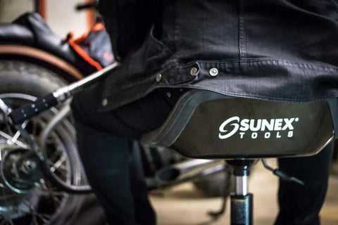Person sitting on Sunex Tools telescoping tractor seat with parts tray, showcasing adjustable height from 18 to 22 inches