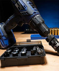 Front view of a cordless drill with a case-trimmer attachment in the chuck beside a black storage case of trimming heads