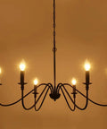 Six Light Farmhouse Chandelier Matte Black Classic Candle Ceiling Fixture with lit bulbs against warm background