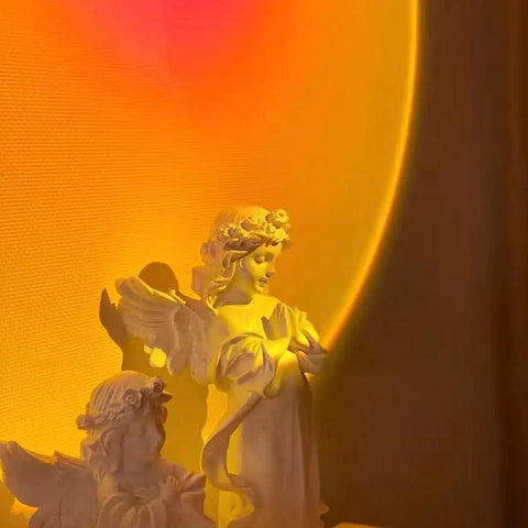 Sunset Projection Lamp With 180 Degree Rotation LED Night Light For Photography And Selfies casting warm glow on angel statues