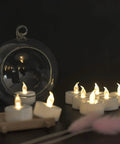 Flameless LED Tea Lights 50 Pack With 200 Hour Battery Realistic Flicker Warm White Glow Battery Operated Candles For Halloween Weddings Parties Seasonal Decor And Ambience. Display with glass holder showcasing warm white LED tea lights on a dark surface.