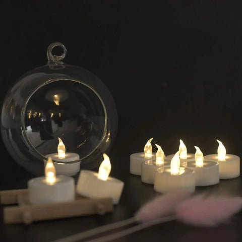 Flameless LED Tea Lights 50 Pack With 200 Hour Battery Realistic Flicker Warm White Glow Battery Operated Candles For Halloween Weddings Parties Seasonal Decor And Ambience. Display with glass holder showcasing warm white LED tea lights on a dark surface.