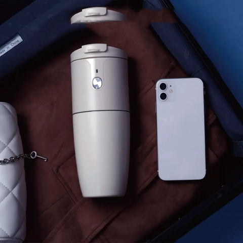 Compact Portable Coffee Maker With Built In Automatic Bean Grinder For Home Desk Or Road Trip next to a smartphone in a suitcase.
