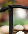 Close-up of black irrigation stake holding drip tubing above pebbles, part of 50 Pack Irrigation Stakes For Quarter Inch Drip Tubing Keeps Drip Lines Off Ground Prevents Clogs Easy Install For 4mm And 7mm Hose Secures Tubing In Place And Lets You Move And Reconfigure Your Drip System On The Fly