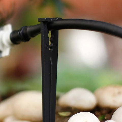 Close-up of black irrigation stake holding drip tubing above pebbles, part of 50 Pack Irrigation Stakes For Quarter Inch Drip Tubing Keeps Drip Lines Off Ground Prevents Clogs Easy Install For 4mm And 7mm Hose Secures Tubing In Place And Lets You Move And Reconfigure Your Drip System On The Fly