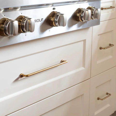 Set Of 12 SleekTouch Antique Brass Cabinet Pulls, 3 3/4 Inch Center To Center installed on white kitchen drawers near stove