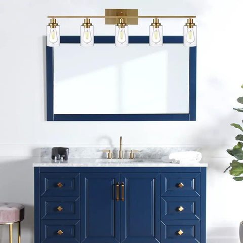 Cool Five Light Brushed Brass Vanity Light Fixture With Clear Glass Shades above a blue bathroom cabinet.