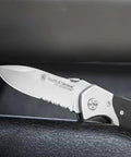 Knockout 8 Inch Folding Knife Packing A 3.3 Inch Drop Point Serrated High Carbon Stainless Blade And G10 Grip Handle on a surface.
