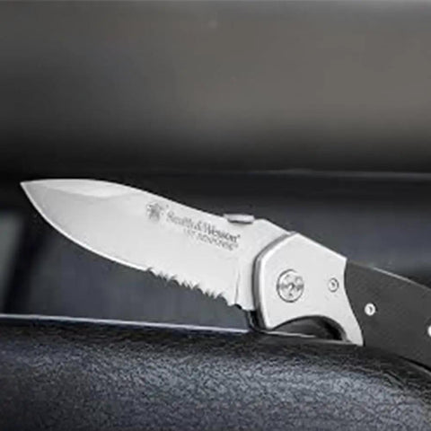 Knockout 8 Inch Folding Knife Packing A 3.3 Inch Drop Point Serrated High Carbon Stainless Blade And G10 Grip Handle on a surface.