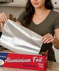 Woman using Heavy Duty Aluminum Foil Roll With Sturdy Corrugated Cutter Box For Thick Food Safe Wrap in kitchen