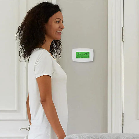 Woman near wall-mounted RTH7600D 7-Day Programmable Touchscreen Thermostat with Home and Away Temperature Settings, white finish.