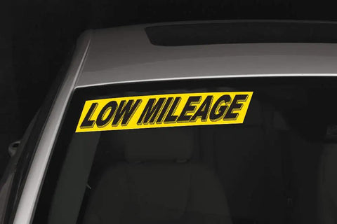 Close-up of a car windshield featuring Ultra High Visibility Car Dealership Window Decals in Bold Black and Yellow Vinyl reading 'LOW MILEAGE'.