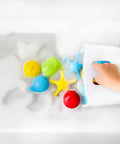 Child’s hand using the Freestanding Bath Toy Drying Bin With Quick Drain Base in soapy water to organize colorful bath toys.