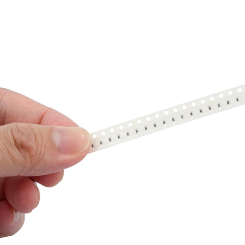 SMD resistor strip on white carrier tape (1206 size) held by fingers.