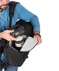 Man accessing camera gear from All Weather Camera Backpack With Padded 15.6 Inch Laptop Compartment, High Capacity SLR Shoulder Bag