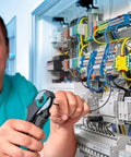 Electrician working on circuit panel with tools in hand.