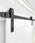 Your Go To Sliding Barn Door Roller Hardware Kit With J Shape Design in frosted black finish installed on a white door