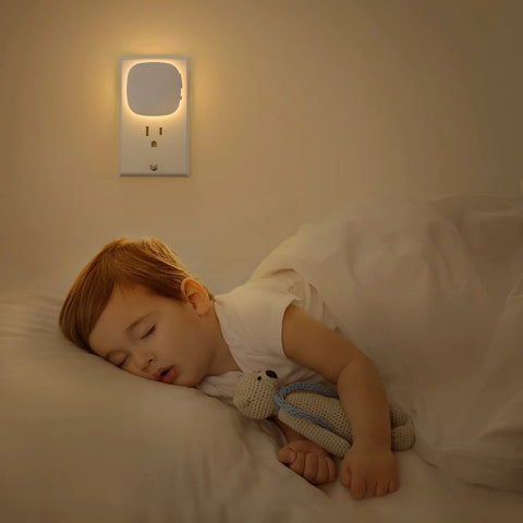 AUVON plug-in LED night light installed in wall outlet; white plastic, warm backlit glow with motion and dusk-to-dawn sensor.