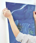 Person installing Part Of Your World The Little Mermaid Peel And Stick Wall Mural By RoomMates on a wall, showing texture and colors.