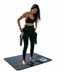 Person standing on a 4mm Neoprene Waterproof Changing Mat 36x30 Inch Portable Wetsuit Changing Pad with Mesh Storage Bag.
