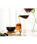 Heavy Duty Dutch Cold Brew Coffee Maker With Solid Wood Tower And Stainless Steel Filter brewing iced coffee into a glass.