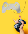 Person holding a black controller under a silver Gamer Neon Sign With 7 Color Changing Mirror LED Backlight Design Luminous Wall Sign For Game Room Decor Cool Teen Bedroom Wall Lamp And Video Game Decor on yellow wall.