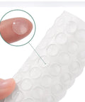 100 Pieces Clear Self Adhesive Cabinet Door Bumpers 0.4 Inch Diameter Rubber Dots Non Slip Soft Close Pads on fingertip close-up.