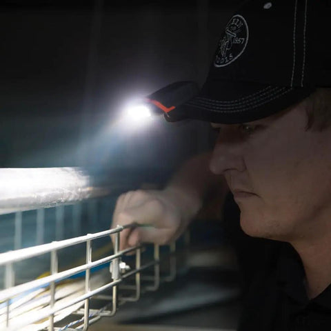 Person wearing Cap Visor Clip LED Light With Pivoting Head, Battery-Powered 2xAAA, inspecting a wire fence at night.