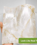 Hand holding Peel And Stick Brown Marble Backsplash Tiles 50 Piece Set 5.9 Inch Square Self Adhesive PVC Wall Tile Decals