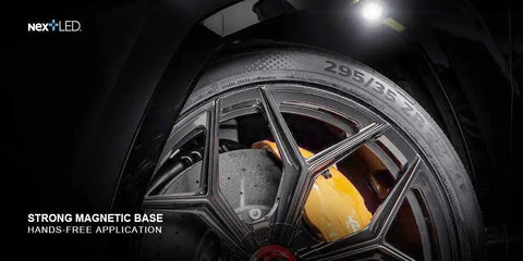 Rechargeable Slim LED Work Light With Clip illuminating a car tire, showing strong magnetic attachment on rugged cast aluminum body