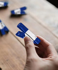 Hand holding a blue metal 2 inch mini spring clamp, part of the 2 Inch Mini Spring Clamps Set Of 30 Heavy Duty Metal Clips For Backdrops