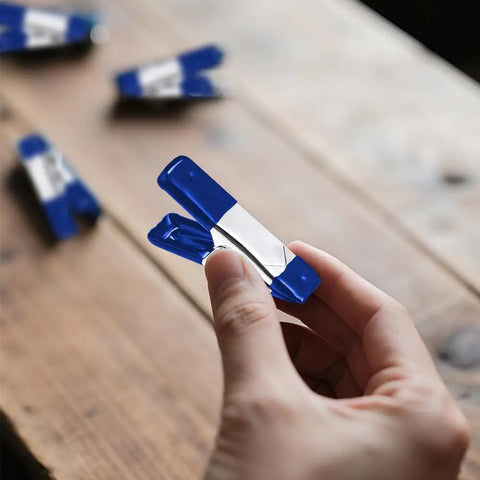 Hand holding a blue metal 2 inch mini spring clamp, part of the 2 Inch Mini Spring Clamps Set Of 30 Heavy Duty Metal Clips For Backdrops