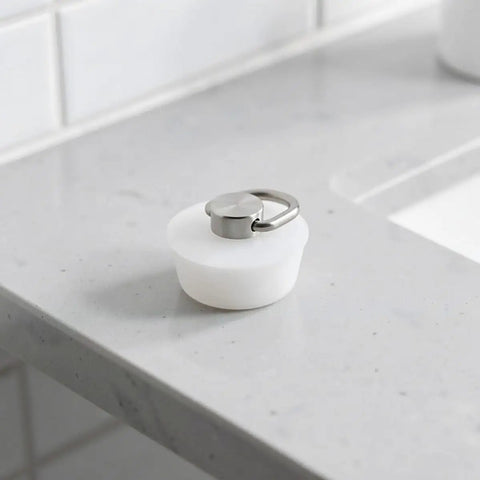 White Silicone Drain Stopper with Ring for Bathtubs and Sinks on a marble countertop, showcasing its elegant design and practicality.