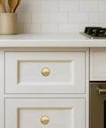 Brushed brass cabinet knobs on white kitchen drawers, showcasing 20 Pack Brushed Brass Cabinet Knobs Heavy Duty Zinc Alloy Bifold Closet Door Hardware Built Tough for Kitchen Cabinets and Bathrooms Fingerprint Resistant Champagne Bronze Finish.