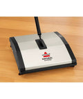 Lightweight Manual Carpet And Hard Floor Sweeper Featuring Dual Rotating Brush Roll Plus Corner Edge Brushes on wooden floor.