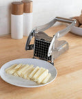 French fry cutter, stainless steel with grid blade, on wooden counter beside plate of sliced potatoes.