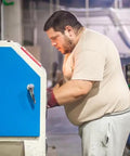 Person using a blue industrial sandblasting machine, possibly utilizing Pro Grade Glass Bead Sandblasting Media For Rust Paint And Dirt Removal 20 To 30 Mesh Medium Large Size 1 Pound Bag Delivers Gentle Surface Cleaning And Smooth Prep For Painting Bonding.