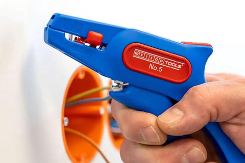 Close-up of a hand using the Automatic Wire Stripper No 5 with Side Cutter for 0.2 to 6 mm2 cables on a wire, orange background.
