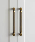 Front view of Six Pack 5 Inch Center To Center Antique Brass Cabinet Pulls With Knurled Grip And Circular End Caps on white doors.