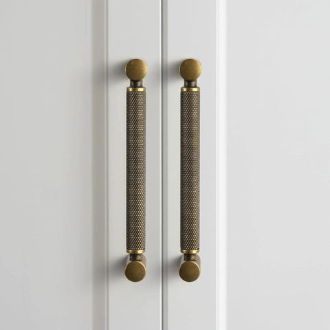 Front view of Six Pack 5 Inch Center To Center Antique Brass Cabinet Pulls With Knurled Grip And Circular End Caps on white doors.