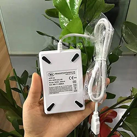 Hand holding an ACR122u A9 Dope Reader Writer For Rewritable UID Changeable Cards with cable against a leafy background.