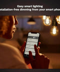 Person using smartphone to control Smart 60W ST19 Filament LED Bulb 2 Pack Soft Warm White 550LM E26 Indoor Lighting With Hue App