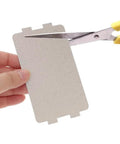 Microwave Waveguide Cover Made From Mica Sheet Heat Resistant Thermal Insulation Pad being cut with scissors, 4.57 by 2.56 inches.