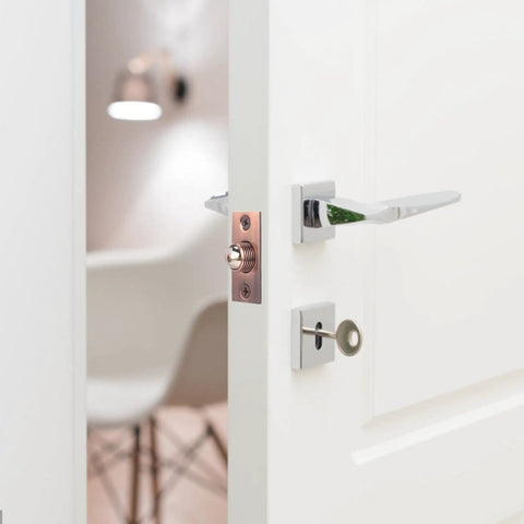 Adjustable pink brass door catch with roller beads on a white door, showcasing heavy duty lock for cupboards.