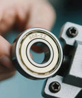Close-up of 100 Pack 608 ZZ Deep Groove Ball Bearings With Double Metal Shields 8mm x 22mm x 7mm being held next to machinery part.