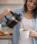 Woman pouring coffee from 12 Ounce Glass French Press Coffee And Tea Brewer For Single Cup Brews Easy To Use With Durable Heat Resistant Glass And Plastic Exterior Reusable Mesh Filter And Smooth Pour Spout Compact 7 Inch Tall into a white mug