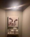 Room corner with activated 2 Pack Battery Powered LED Puck Lights With Remote For Lamps And E26 Screw In Fixtures lighting a painting.