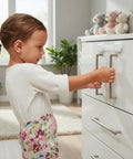 Child interacts with baby proofing and kid proofing essentials outlet covers cabinet locks drawer safety latches door stoppers and strap locks white 6 pack to keep curious toddlers safe in cabinets drawers kitchen fridge and more on a white cabinet