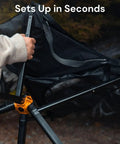 Person setting up an Ultra Compact Portable Camp Chair in black that folds to bottle size, depicted mid-assembly outdoors.