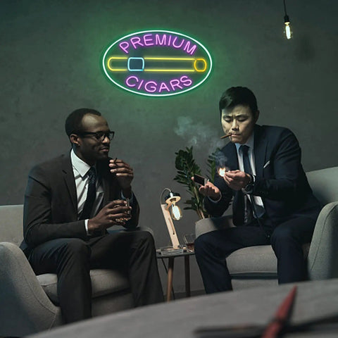 Two men smoking cigars beneath a Premium Cigars neon sign in a lounge setting, enjoying a relaxed atmosphere.